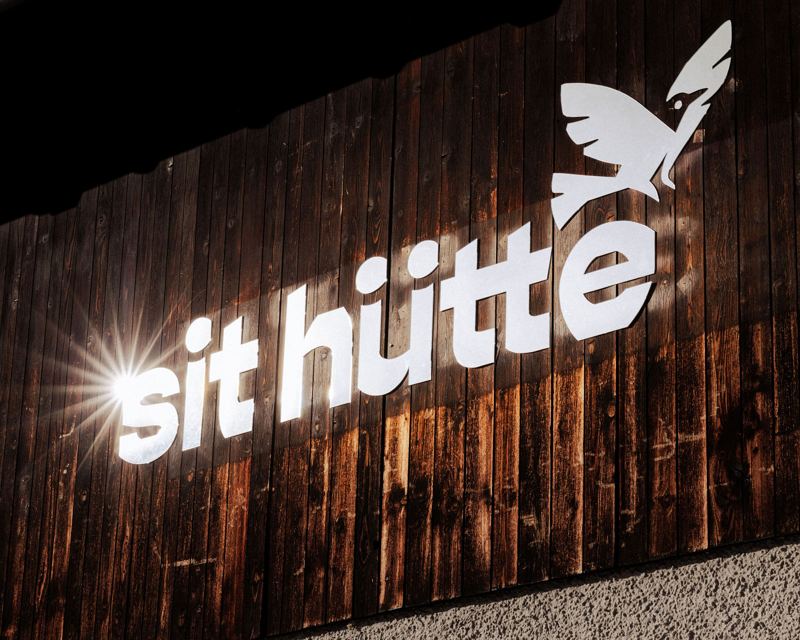 Beleuchteter sit-hütte-Schriftzug auf Holzfassade bei Nacht