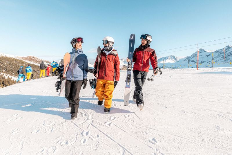 Drei Snowboarder laufen im Sonnenschein zur Hütte