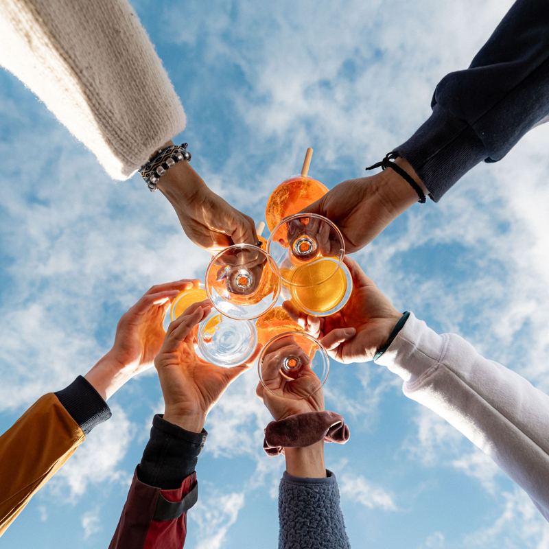 Anstossen mit Aperol vor blauem Himmel, von unten fotografiert