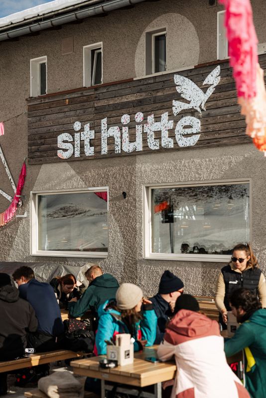 Volle Terrasse vor der Fassade mit sit-hütte-Schriftzug