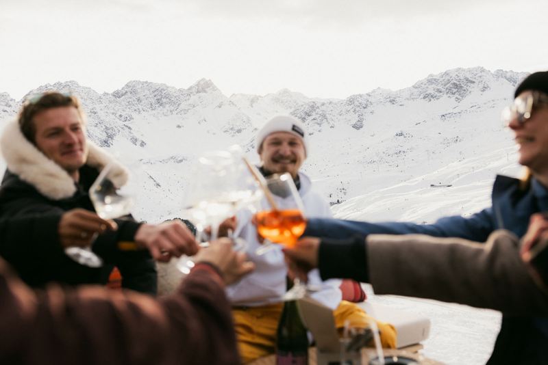 Freunde stossen auf der Terrasse an, dahinter die Berge