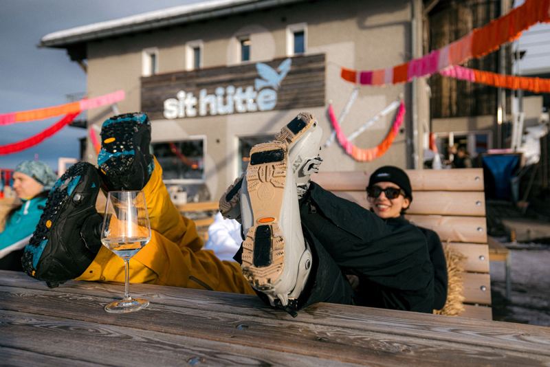 Gäste entspannen mit Skischuhen auf der Terrasse vor der Hütte